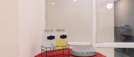 A room with a red patterned tablecloth, two beverage dispensers, and a tray of glasses.