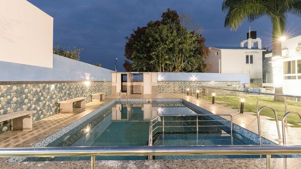 Una piscina con pared de piedra, bancos y una palmera.