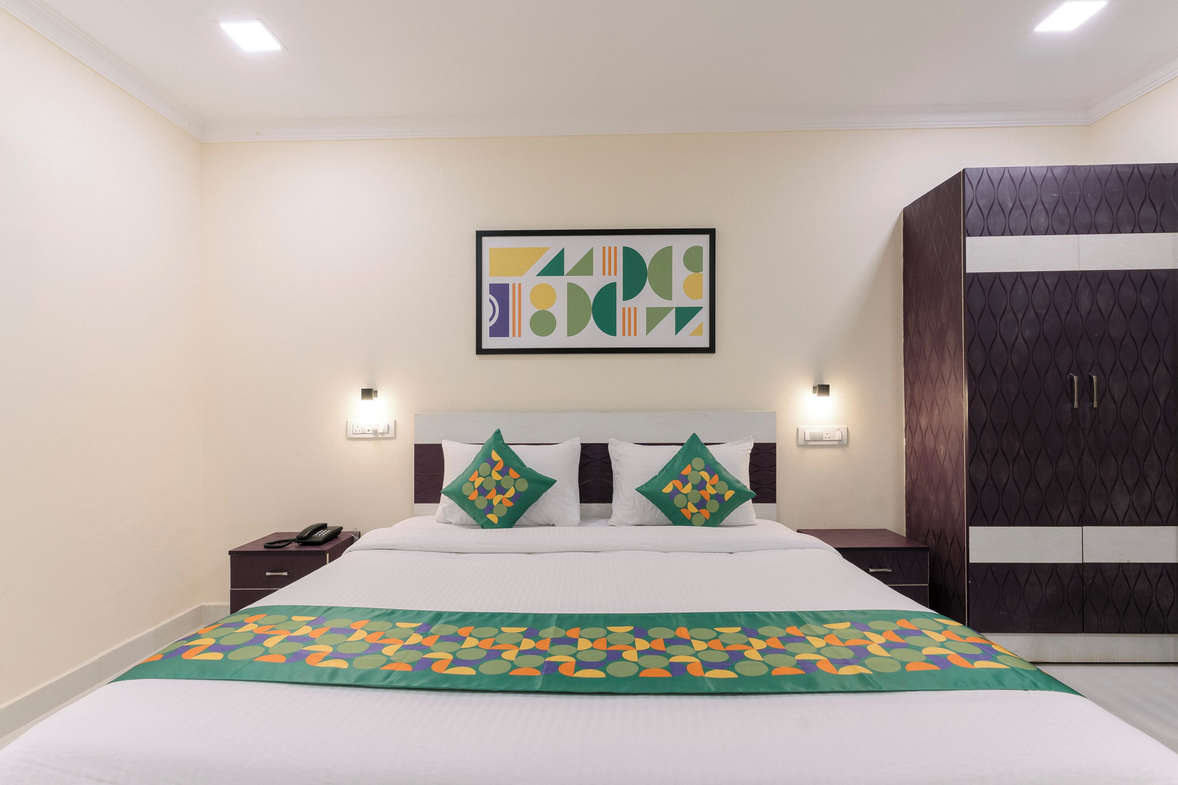 A hotel room with a bed, two bedside tables, a wardrobe, and a wall-mounted abstract art piece.