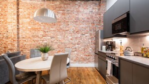 A modern kitchen with a brick wall, a dining area with a table and chairs, and a built-in oven. - Hollyhock Suite 503: 2 bed/1 bath (Louisville)