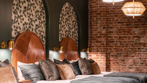 A modern bedroom with a large bed, two side tables, and a brick wall. - Hollyhock Suite 504: 1 bed/1 bath (Louisville)