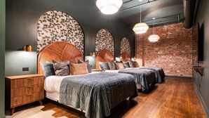 A modern hotel room with a brick wall, a large bed with a wooden headboard, two bedside tables, and a large mirror. - Hollyhock Suite 504: 1 bed/1 bath (Louisville)