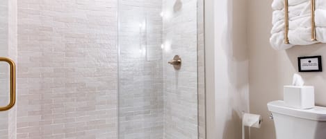 Casa de banho moderna com chuveiro em cabine de vidro, sanita branca e barra para toalhas.