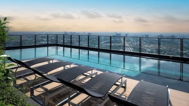 Ein Rooftop-Endlospool mit Liegestühlen, umgeben von einem Glasgeländer und mit Blick auf die Stadt.