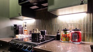 Una cocina con estufa, hervidor y diferentes condimentos sobre la encimera.