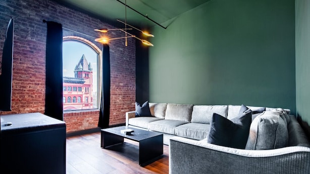 Una sala de estar moderna con un sofá, una mesa de centro y vistas a un edificio rojo a través de un ventanal grande.