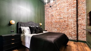 Un dormitorio con pared de ladrillo, una cama con ropa de cama negra, una mesita de noche y una lámpara moderna.