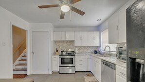 Una cocina moderna con armarios blancos, electrodomésticos de acero inoxidable y un ventilador de techo de madera.