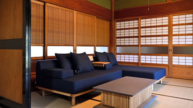 Une pièce de style japonais traditionnel, avec un sol recouvert de tatamis, une basse table en bois et un canapé bleu agrémenté de coussins.