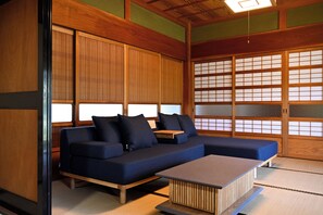 Ein traditioneller japanischer Raum mit Tatami-Boden, einem niedrigen Holztisch und einem blauen Sofa mit Kissen.