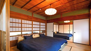Une pièce de style japonais traditionnel, avec un sol recouvert de tatamis, deux lits, des portes coulissantes et un ventilateur de plafond.