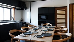 Un espace repas moderne avec une longue table dressée pour six personnes, des chaises en bois et un buffet noir en arrière-plan.