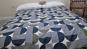 Ein Bett mit einem gemusterten Überwurf, einem weißen Kopfkissen und einem Holzstuhl mit Sitzkissen.