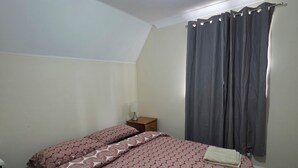 A bedroom with a bed, a nightstand, a lamp, and a window with curtains. - Stay Near Colchester twn centre4 (Colchester)