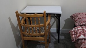 A corner room with a wooden chair, a white table, and a patterned bed. - Stay Near Colchester twn centre4 (Colchester)