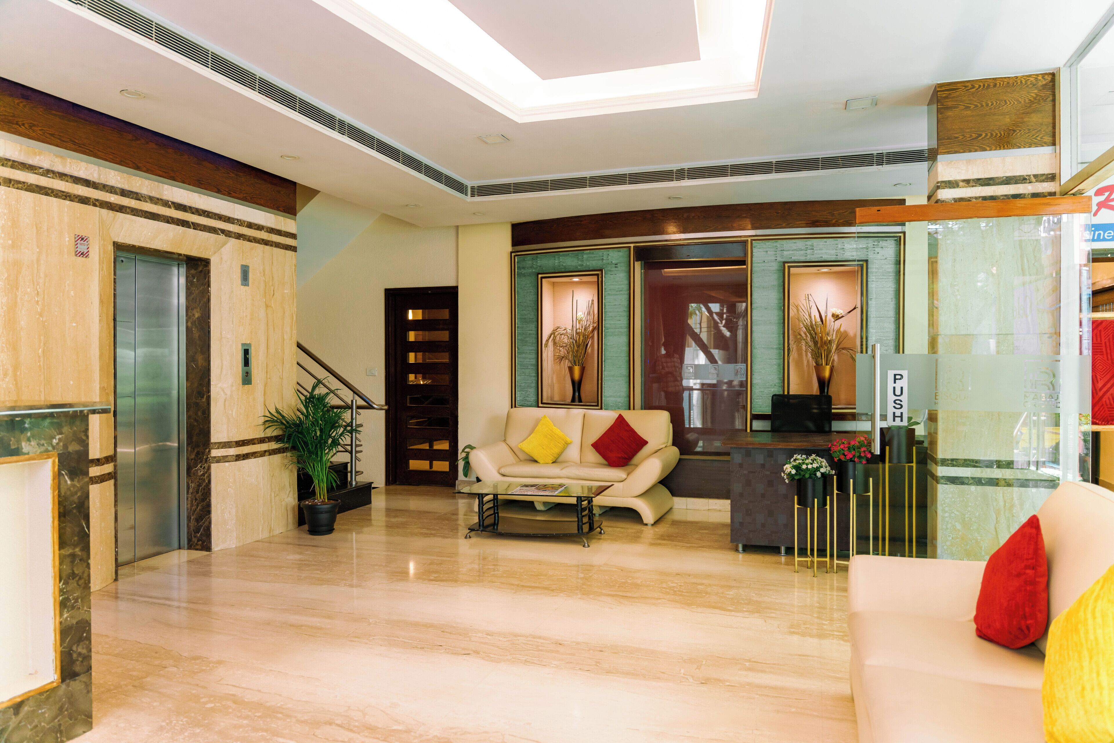 A hotel lobby with a reception desk, a sofa, a staircase, and a potted plant.