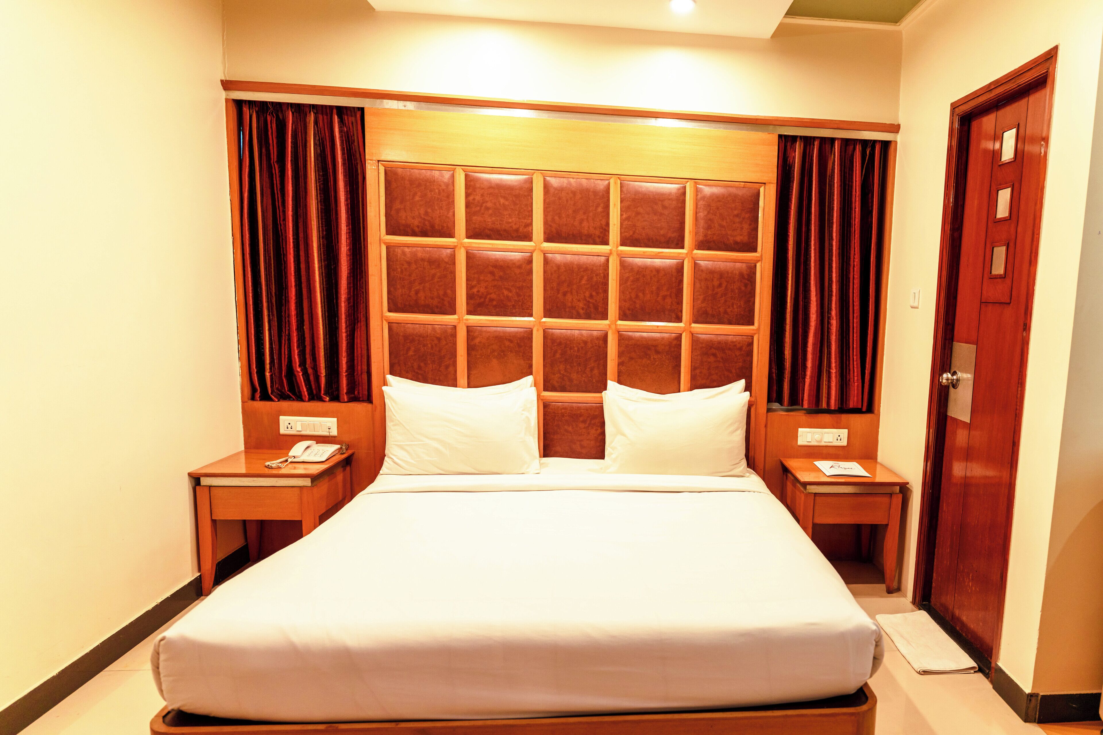 Quarto de hotel com uma cama grande, duas mesas de cabeceira, um painel de cabeceira de madeira e uma porta.
