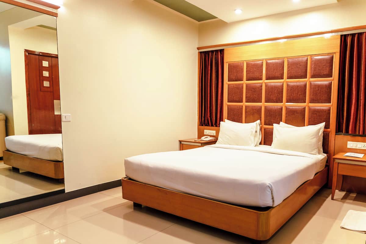 Habitación de hotel con una cama grande, cabecera de madera, dos mesitas de noche y un espejo en la pared.