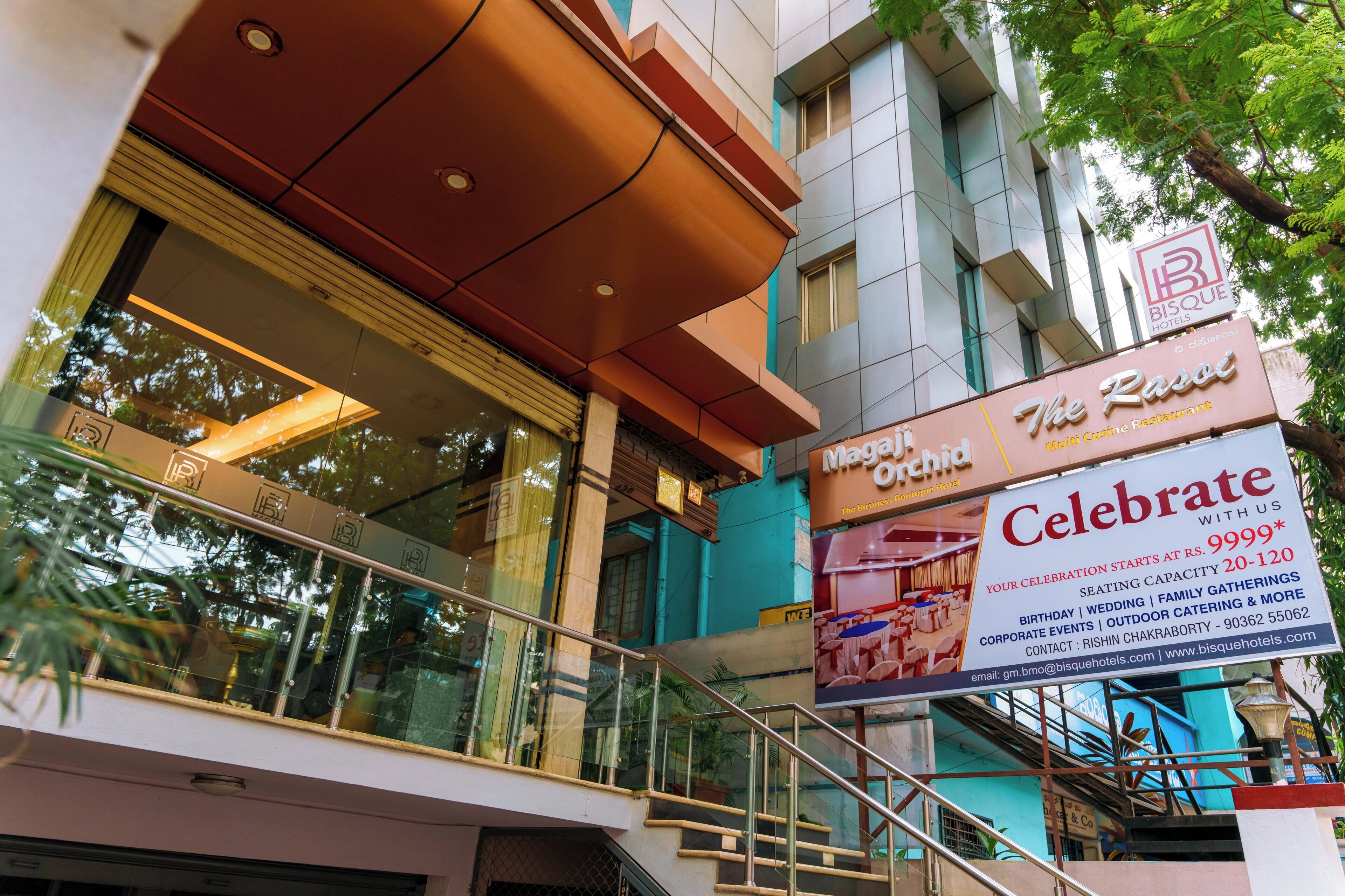 A multi-story hotel with a glass facade, a staircase, and a sign advertising a multi-cuisine restaurant.