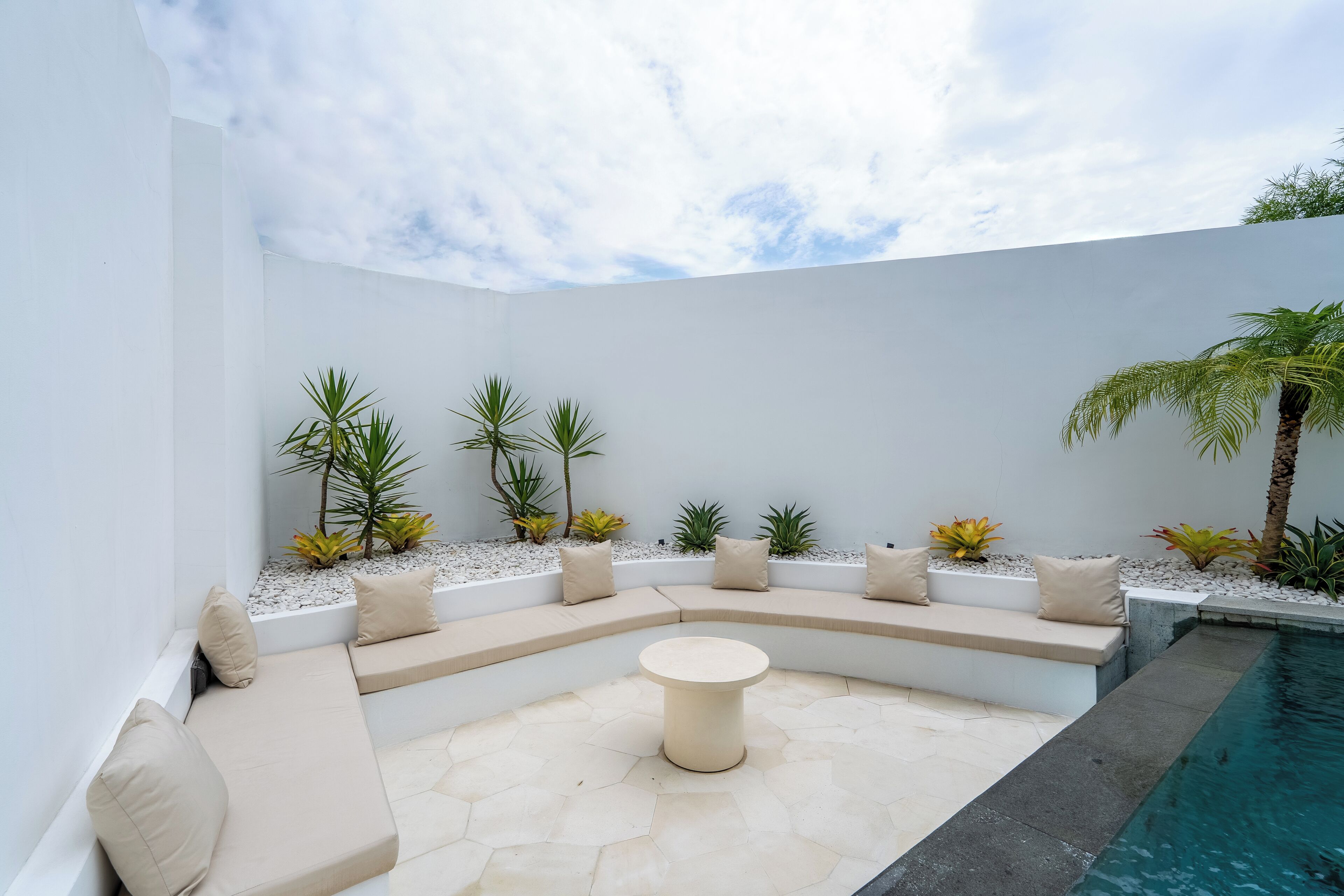 A modern outdoor seating area with a pool, featuring a curved bench with cushions and a central round table.