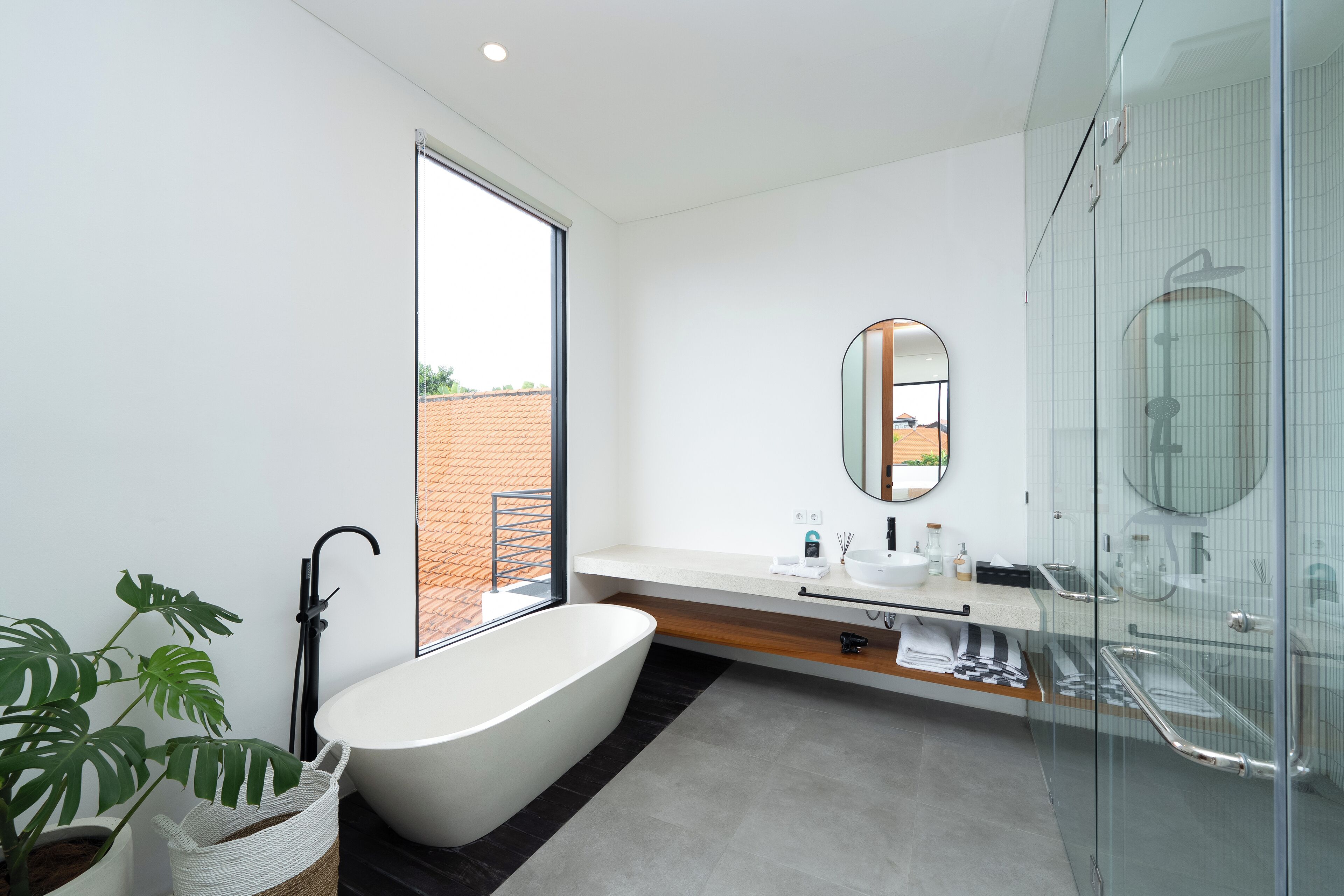 A modern bathroom with a freestanding bathtub, a glass shower enclosure, and a large window offering a view of the outdoors.