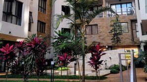 Un edificio residencial de varios pisos con balcones, un patio con plantas y un muro de piedra.