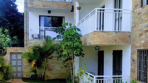 Un edificio de varios pisos con balcones, un sendero pavimentado y un jardín cuidado.