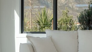 A modern living room with a white sofa, a wooden coffee table, and a large window offering a view of a mountainous landscape. - Private Spa with Remarkables & Coronet Views (Jacks Point)
