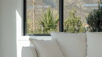 A modern living room with a white sofa, a wooden coffee table, and a large window offering a view of a mountainous landscape.