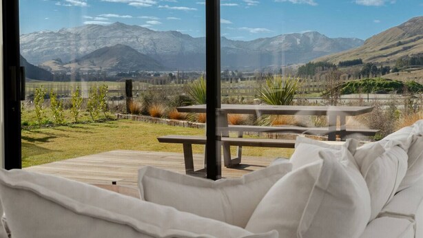 A room with a large window overlooking a mountainous landscape, a wooden deck, and a white sofa. - Private Spa with Remarkables & Coronet Views (Jacks Point)