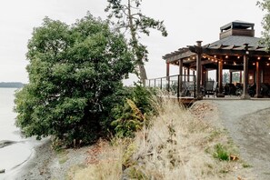 Une structure en bois située au bord du lac, dotée d’un espace extérieur avec des sièges et d’une terrasse couverte.