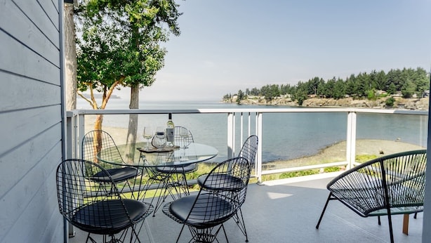 Un balcon avec une table et des chaises, donnant sur une étendue d’eau et une zone boisée.