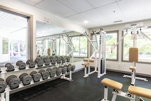 A gym with weightlifting equipment, dumbbells, benches, and a window with a view of the outdoors.