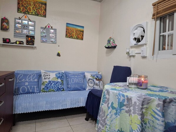 Une pièce comprenant un canapé, une table avec une bougie et des éléments de décoration murale, notamment un tableau représentant un tournesol et une photographie encadrée.