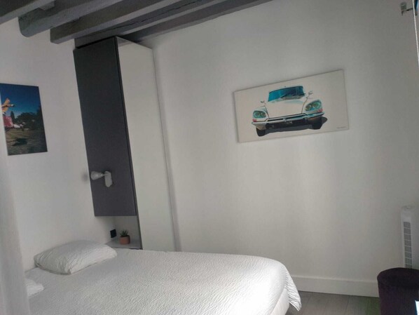 Un dormitorio con cama, una puerta, un estante con planta y una ilustración de coche en la pared.