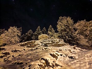 A snow-covered landscape with a building on a hill, surrounded by trees.