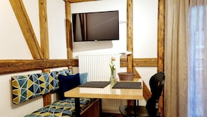 A cozy room with a wooden bench, a table, a chair, a TV mounted on the wall, and a radiator.