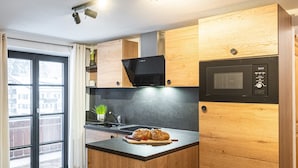 Moderni keittiö, jossa on puiset kaapit, musta mikroaaltouuni ja pieni keittiösaareke, jossa on leikkuulauta ja leipää.