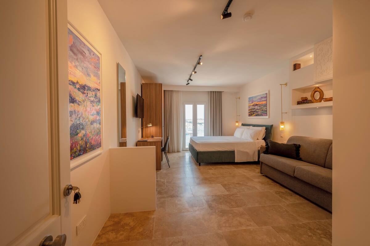 Una habitación de hotel con cama, sofá, escritorio y un cuadro en la pared.