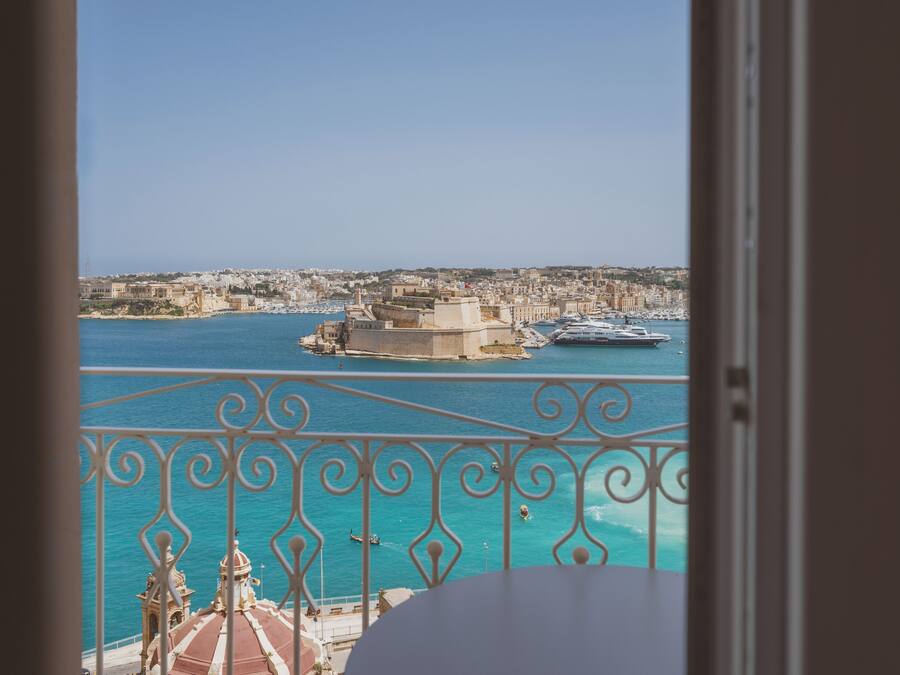 Un balcón con vistas a un pueblo costero, un puerto con barcos y un edificio destacado con una cúpula.