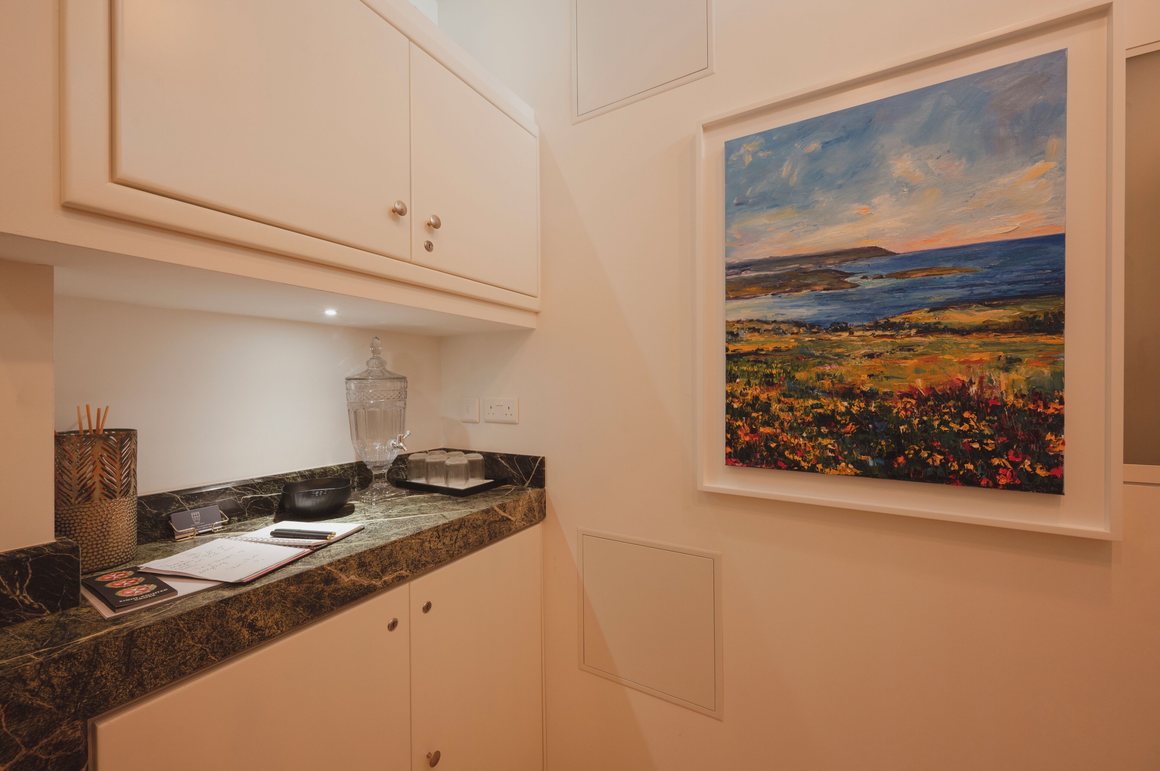 Una cocina con armarios blancos, una encimera de granito y un cuadro de un paisaje en la pared.