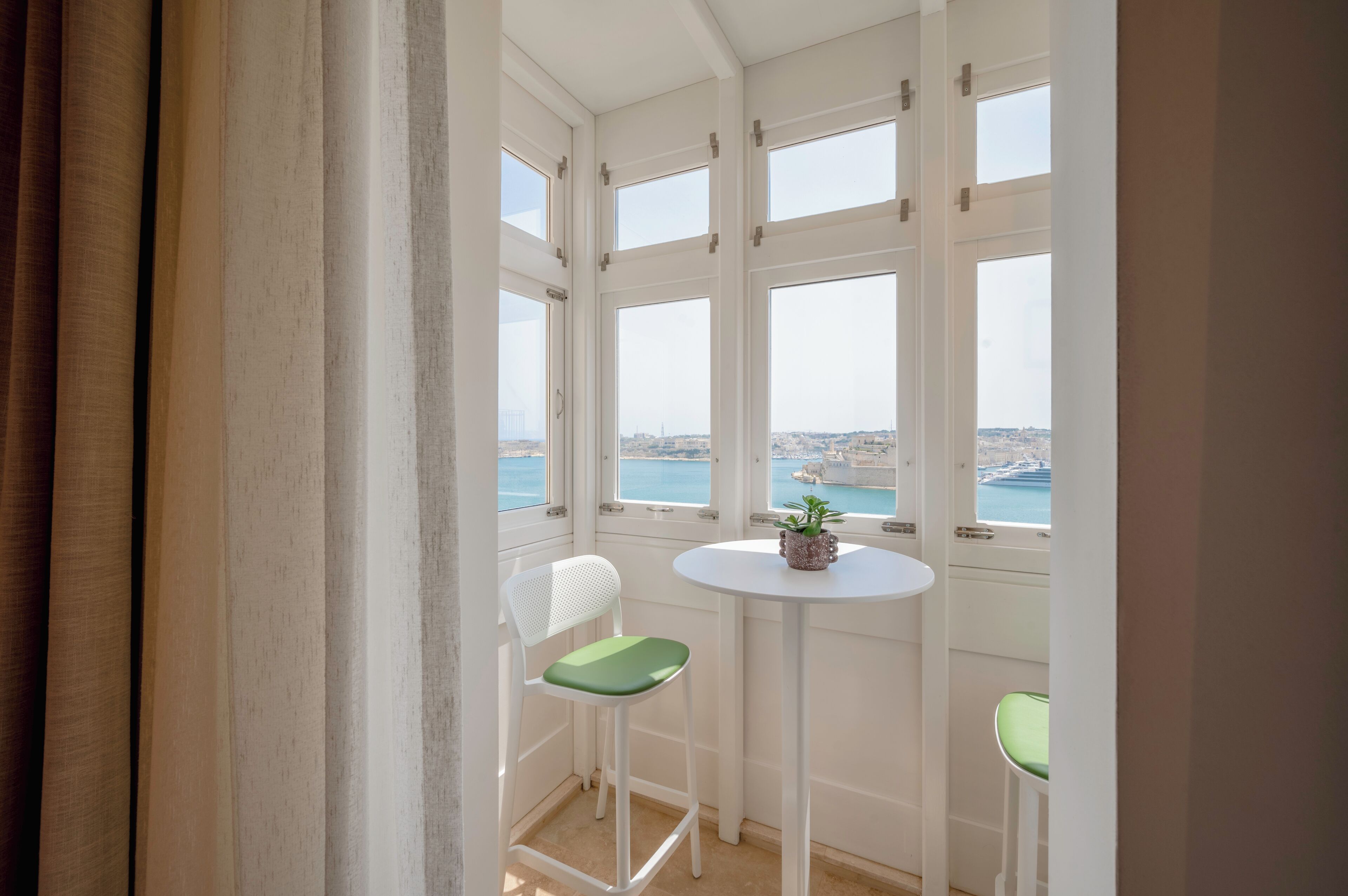 Een balkon met uitzicht op zee, een tafeltje met een plantje en twee stoelen.