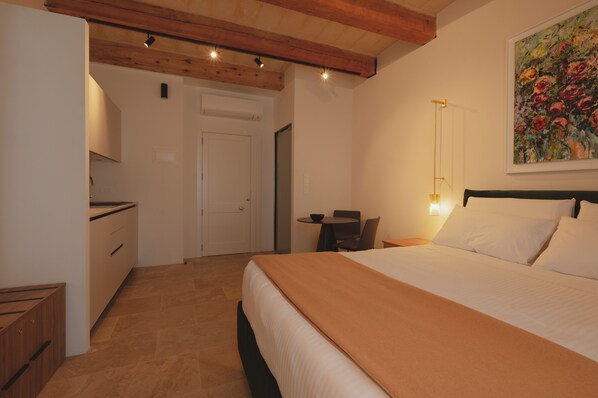 A bedroom with a bed, a desk, and a chair. There is a door leading to another room. - V60 Valletta (Valletta)