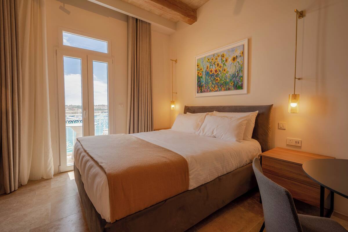 Habitación de hotel con cama, escritorio, silla, un cuadro y vistas por la ventana.