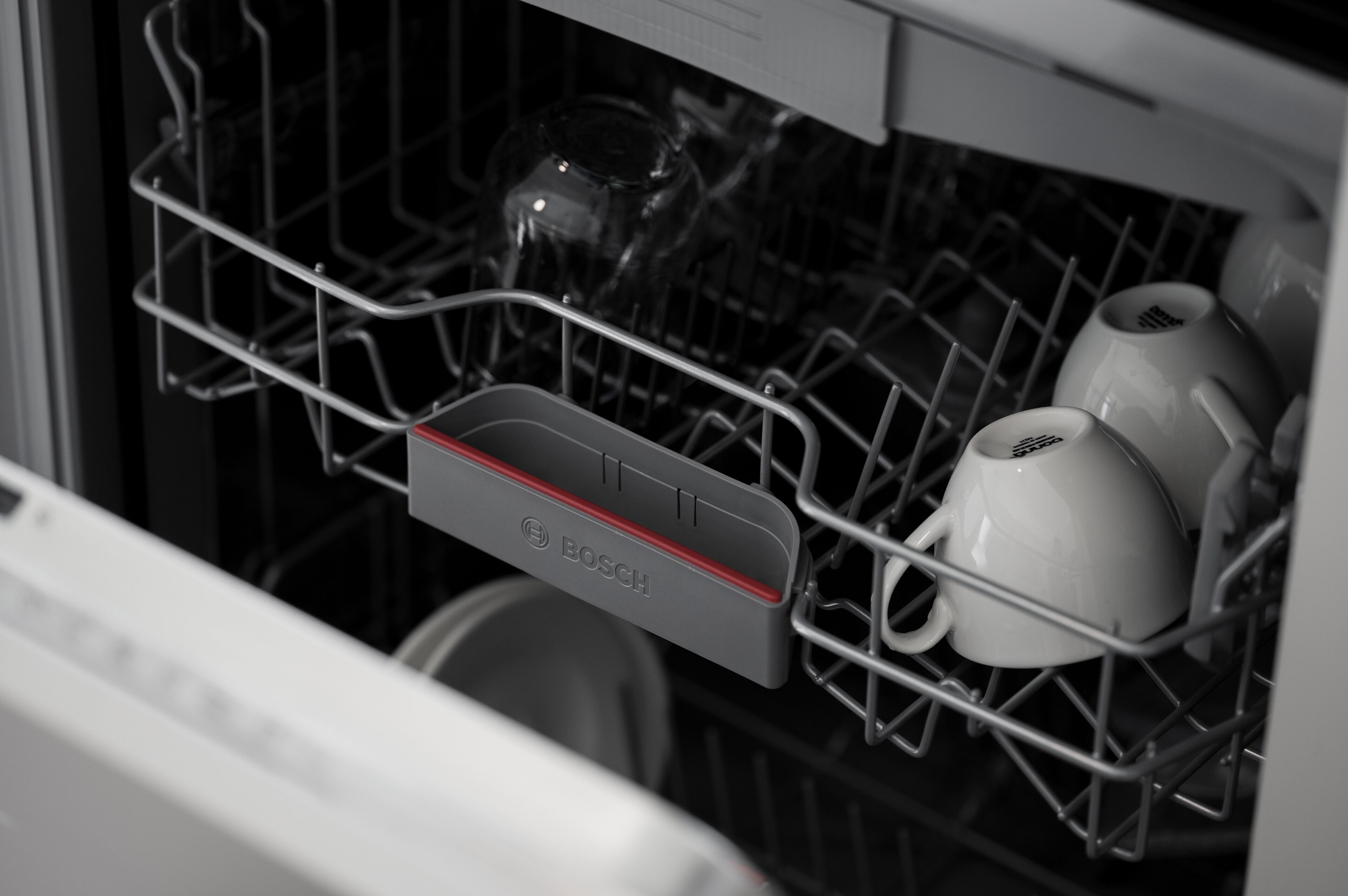 A Bosch dishwasher with a metal rack holding cups and a glass.