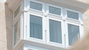 Ein Gebäude mit einem Balkon, verziert mit aufwendigen Metallgeländern, und einem Fenster mit Vorhang.