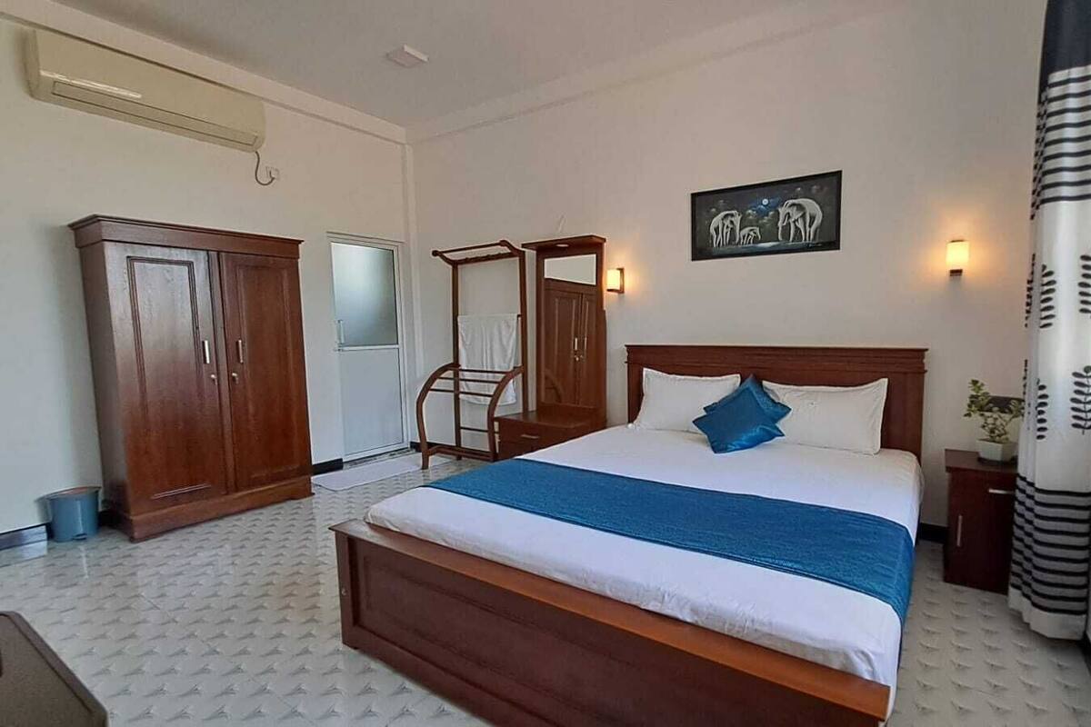 A bedroom with a large bed, a wardrobe, a bedside table, and a wall-mounted artwork.