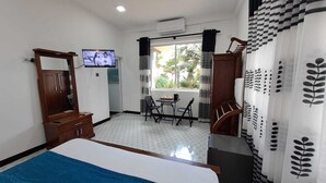 A hotel room with a bed, a TV, a desk with a chair, and a window with curtains. - Mario Ocean View (Uswetakeiyawa)