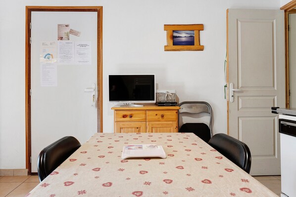 A small room with a dining table, chairs, a television, and a refrigerator.