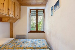 A bedroom with a bed, a window, wooden ceiling, and a wall-mounted picture.